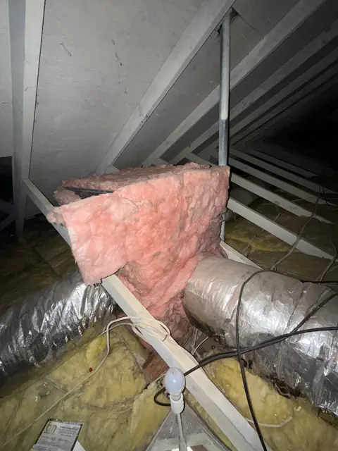 Insulated flexible duct and a pink duct wrap running along an attic floor