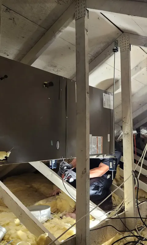 A technician working beneath a unit hung in an attic
