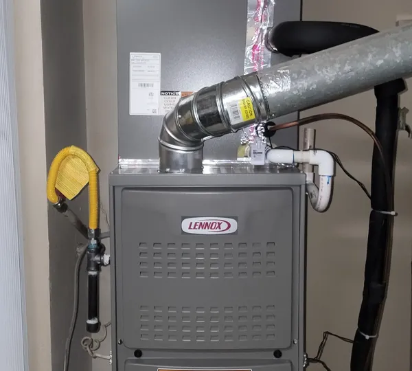 A furnace in an alcove with its vent pipe and a flexible duct above it
