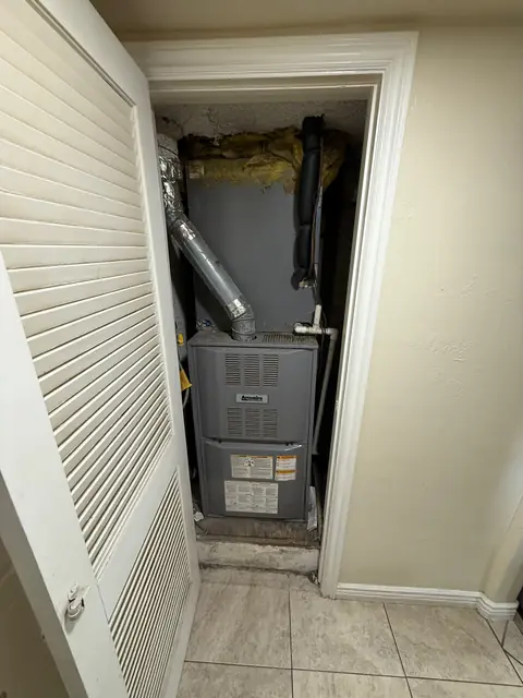 A furnace in a utility closet seen through its open louvred door