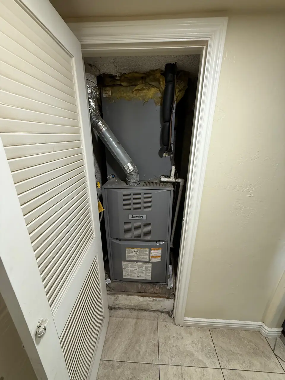 A furnace in a utility closet, seen through its open louvred door