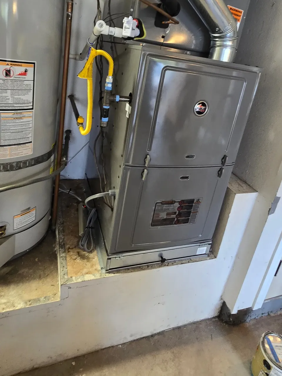 A gas furnace with its vent pipe, set beside a water heater